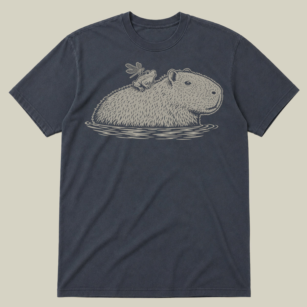 A dark slate blue crewneck t-shirt featuring a detailed line art graphic of a capybara in water with a frog perched on its back, displayed against a solid light beige background.