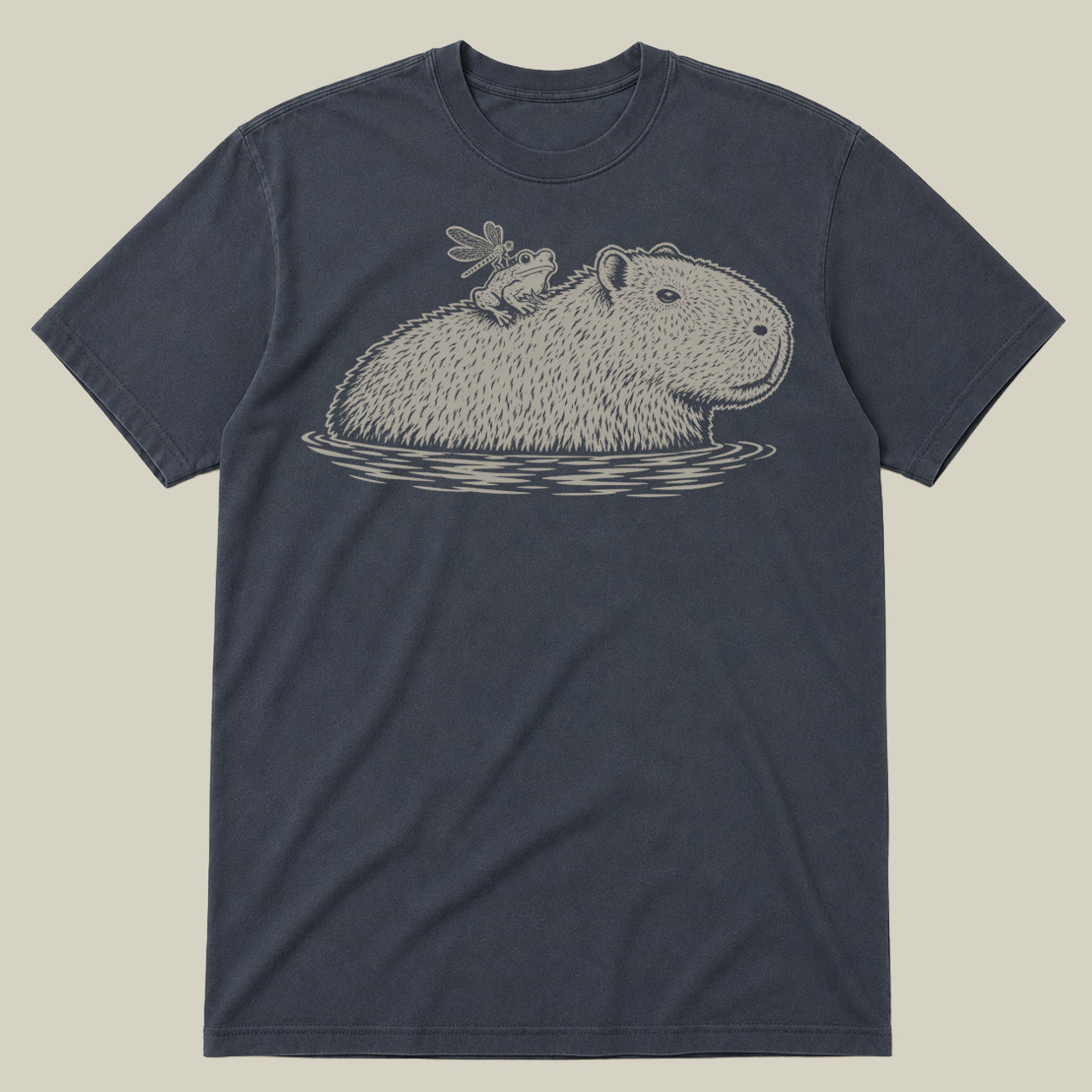 A dark slate blue crewneck t-shirt featuring a detailed line art graphic of a capybara in water with a frog perched on its back, displayed against a solid light beige background.